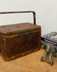The Woven Rectangular Picnic Basket with Handle & Hinged Lid sits on a wooden surface beside stacked books and a small metal elephant figurine, showing off exquisite Southeast Asian craftsmanship.