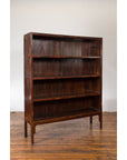 Dark wood Chinese Qing Dynasty bookcase with four shelves, 19th century, on wooden floor by white brick wall.