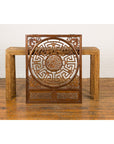 Brown wood fretwork panel with phoenix, bats, and geometric maze design, displayed in front of a woven table.