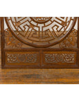 Brown wooden Qing Dynasty fretwork panel with phoenix, bats, and geometric maze on wood floor against white brick wall.