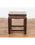 Brown lacquered wood low table with carved apron and horse hoof legs, set on wooden floor against a white wall.