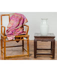 Brown wooden chair with patterned fabric next to a Qing Dynasty brown lacquer low table with carved apron and hoof legs.