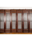 Black lacquered wood six-panel Qing Dynasty screen with carved meander motifs, set against a white wall and wood floor.