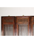 Black lacquered wood six-panel Qing Dynasty screen with carved meander motifs against a white brick wall.