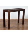 Dark brown rattan console table with midcentury country style on wooden floor against a white brick wall.