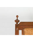 Close-up of brown wood and rattan Dutch Colonial lounge chair with carved finials on a white background.