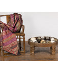 Pink and gold textile on chair beside a 1920s Indian wooden chakki table with hand-carved geometric patterns.