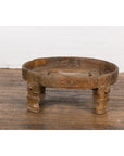 Brown wood antique Chakki grinding table with hand-carved geometric patterns on hardwood floor by white brick wall.