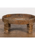 Brown wooden Indian Chakki grinding table with hand-carved geometric details and four legs on a wooden floor.