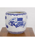 Blue and white porcelain planter with hand painted landscape, displayed on a wooden surface against a white wall.