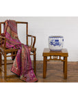 Wooden chair with pink shawl next to table holding blue and white porcelain planter with landscape design.