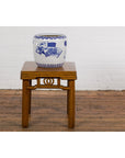 Blue and white porcelain planter with hand painted landscape on wooden stool against white brick wall.