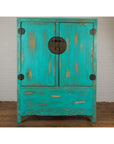 Blue-green lacquered wood Qing Dynasty cabinet with carved apron, set against a white brick wall.