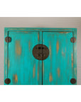 Blue green lacquer wood Qing Dynasty cabinet with carved apron, displayed against a white brick wall.