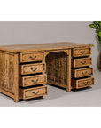 Bleached teak kneehole desk with eight drawers, leafy plant in brown pot visible in background.