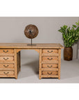 Bleached teak kneehole desk with eight drawers, sculpture on top, and potted plant beside, front view.