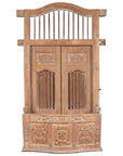 Natural wood balcony window with bonnet top, hand carved foliage motifs, vertical slats, and panel designs.