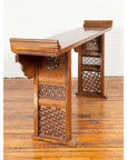 Brown wood Qing Dynasty altar table with bamboo accents, fretwork, and everted flanges against white brick wall on wood floor.
