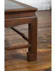 Close-up of brown wood Burmese vintage low coffee table leg and Negora lacquered top on worn wooden floor.