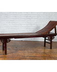 Brown elm and bamboo Qing Dynasty lounge chair with cloud carved spandrels against a white brick wall.