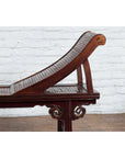 Brown elm and bamboo Qing Dynasty lounge chair with cloud-carved spandrels in front of a white brick wall.
