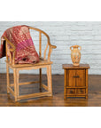 Wooden chair with red throw beside a dark wood Chinese Qing Dynasty 19th-century cabinet with a vase on top.