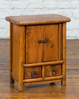 Small brown wood Qing Dynasty bedside cabinet with tapering lines, on wood floor against white brick wall.