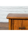 Close-up of a brown wood Qing Dynasty 19th-century bedside cabinet with tapering lines beside white brick wall and wood floor.
