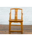 Brown elmwood Chinese Qing Dynasty 19th c. armchair with hand-carved medallion on wooden floor by white brick wall.
