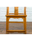 Brown elmwood Qing Dynasty armchair with carved medallion, on wooden floor against white brick wall.