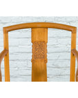 Brown elmwood Chinese Qing Dynasty armchair with carved medallion, placed against a white brick wall.