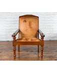 Brown leather Dutch Colonial plantation lounge chair on wooden floor next to a white brick wall.