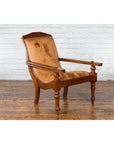 Brown leather and wood Dutch Colonial plantation lounge chair on wood floor against a white brick wall.