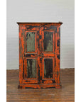 Burnt orange and green hand-painted Indian cabinet on wooden floor against white brick wall.