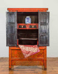 Black lacquer cabinet with open doors, blue-and-white vase on red patterned fabric.