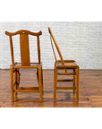 Pair of dark wood Chinese Qing Dynasty 19th century yoke high back chairs, one upright, one tilted, against white brick wall.
