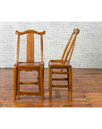 Pair of dark wood Qing dynasty yoke high back chairs on wooden floor against a white brick wall.