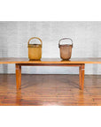 Brown mango wood Indonesian dining table with tapered legs, two tall woven baskets placed beside it, indoor setting.