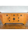 Natural wood Qing Dynasty 19th century sideboard with large carved spandrels, set against a white brick wall.