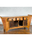 Natural wood Qing Dynasty sideboard with carved spandrels, three drawers, two cabinets, set against white brick wall.