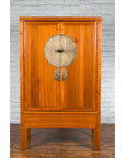 Brown elmwood Chinese Qing Dynasty armoire with medallion hardware against a brick wall, 19th century.