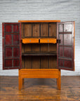 Brown elmwood Qing Dynasty armoire with medallion hardware, doors open, on wood floor by a brick wall.