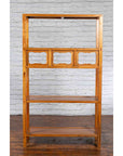 Brown elmwood Qing Dynasty bookcase with three shelves and pierced cartouches against white brick wall, wood floor.