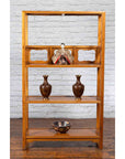 Brown elmwood Chinese Qing Dynasty bookcase with three shelves and pierced cartouches against a white brick wall.