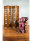 Brown wooden four-panel screen with geometric fretwork motifs next to a wooden chair draped with patterned fabric.