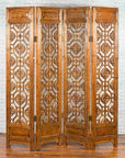 Brown wood four-panel screen with geometric fretwork motifs, set against a white brick wall background.