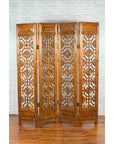 White four-panel screen with geometric fretwork motifs, wood material, on wooden floor by a white brick wall.