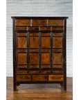 Dark wood Chinese Qing Dynasty armoire with 14 drawers, 2 doors, set against a white brick wall background.