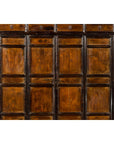 Close-up of dark wood Chinese Qing Dynasty armoire cabinet with 14 drawers, two doors, against a white brick wall.
