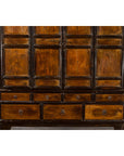 Close-up of dark wood Qing Dynasty Chinese armoire cabinet with 14 drawers and two doors against a white brick wall.
